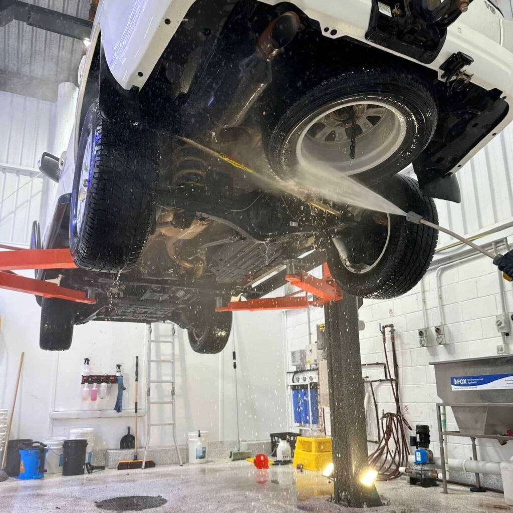 Mechanic spraying protective wax on vehicle undercarriage
